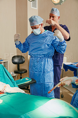 Buy stock photo Shot of two surgeons helping each other get dressed for surgery