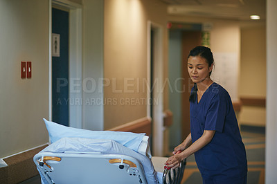 Buy stock photo Cropped shot of a female nurse pushing a hospital bed down the corridor