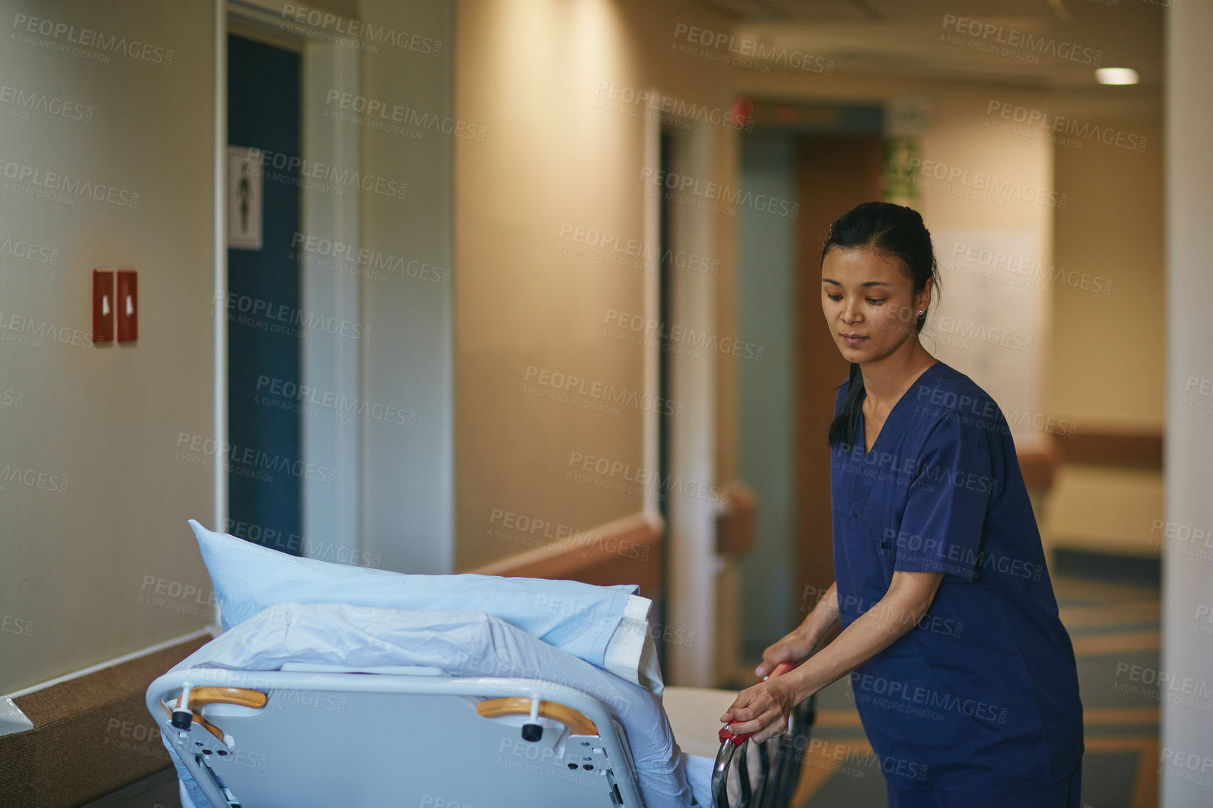 Buy stock photo Cropped shot of a female nurse pushing a hospital bed down the corridor
