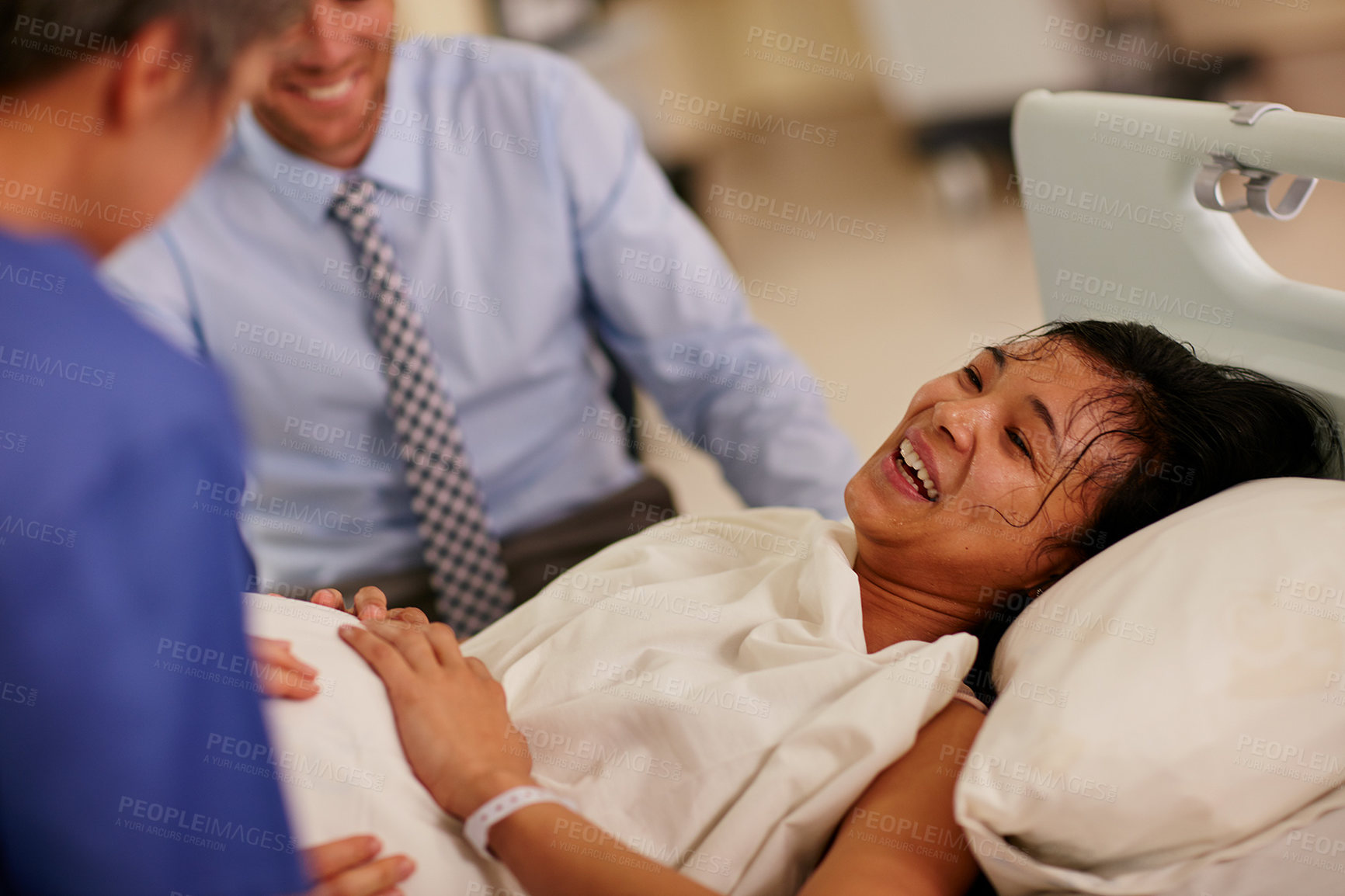 Buy stock photo Shot of a young woman lying in hospital with her husband in the background