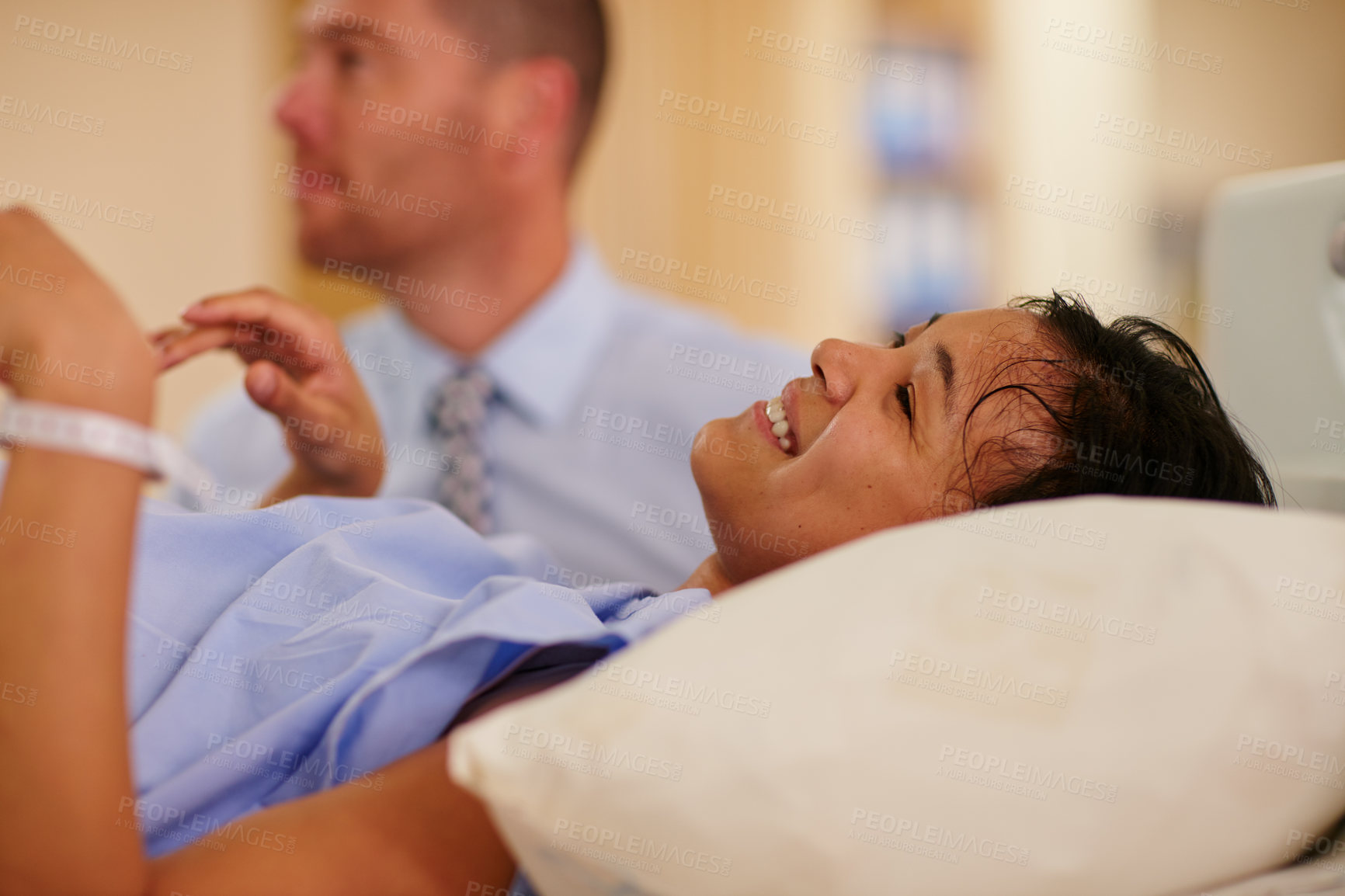 Buy stock photo Shot of a young woman lying in hospital with her husband in the background