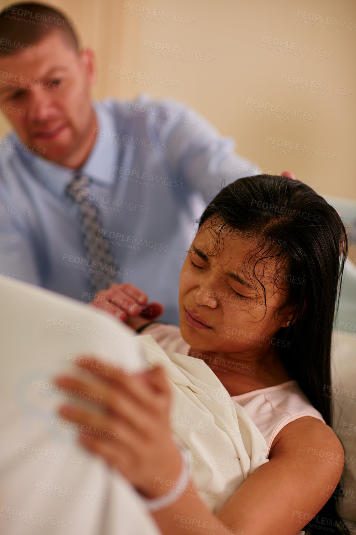 Buy stock photo Shot of a young woman giving birth with her husband supporting her in the background