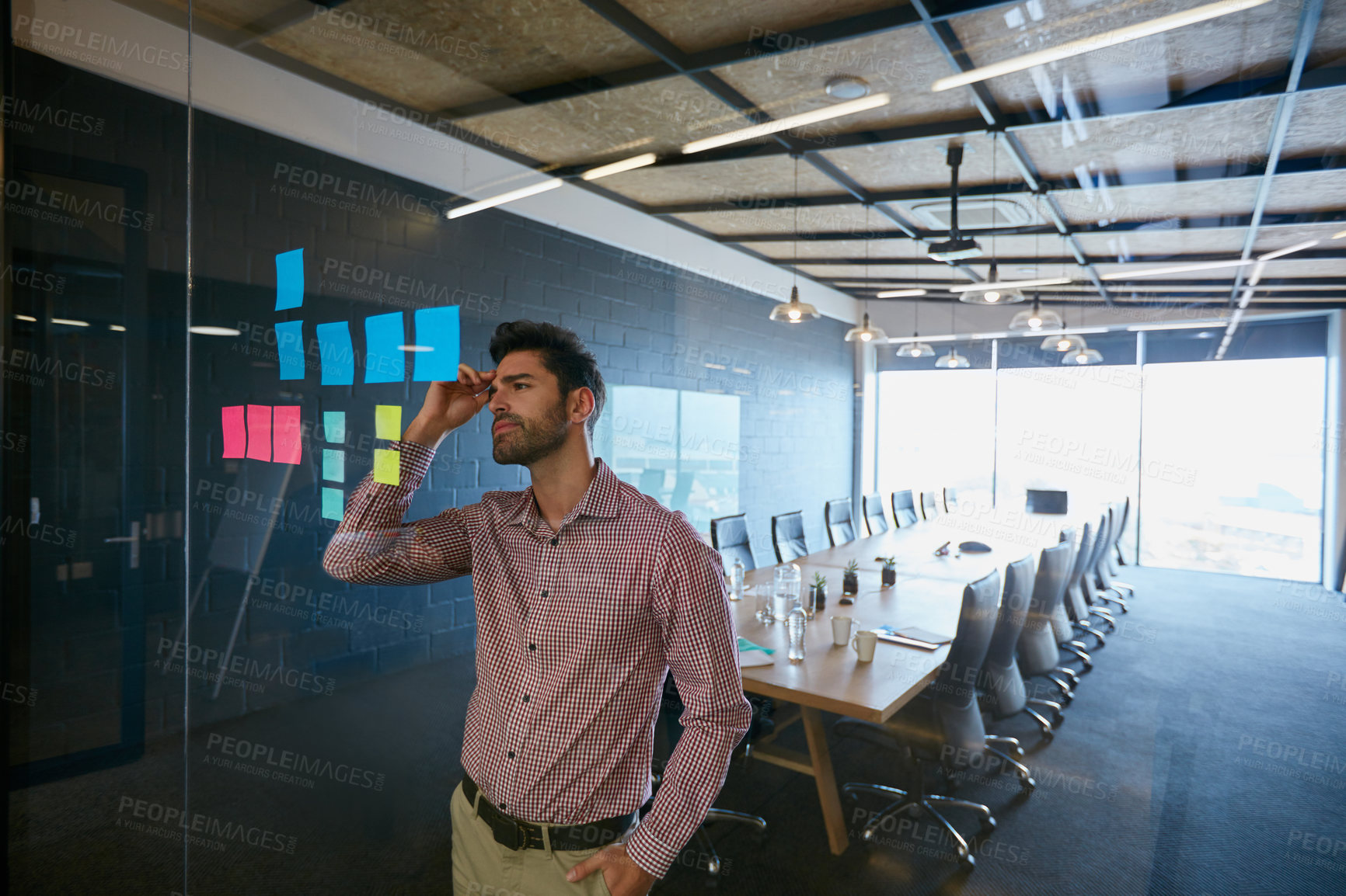 Buy stock photo Shot of a young businessman looking at sticky notes on a glass wall