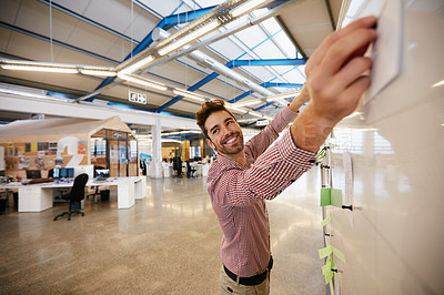 Buy stock photo Shot of a young businessman working on sticky notes on a whiteboard