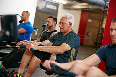 Buy stock photo Cropped shot of a group of men working out on the rowing machine at the gym