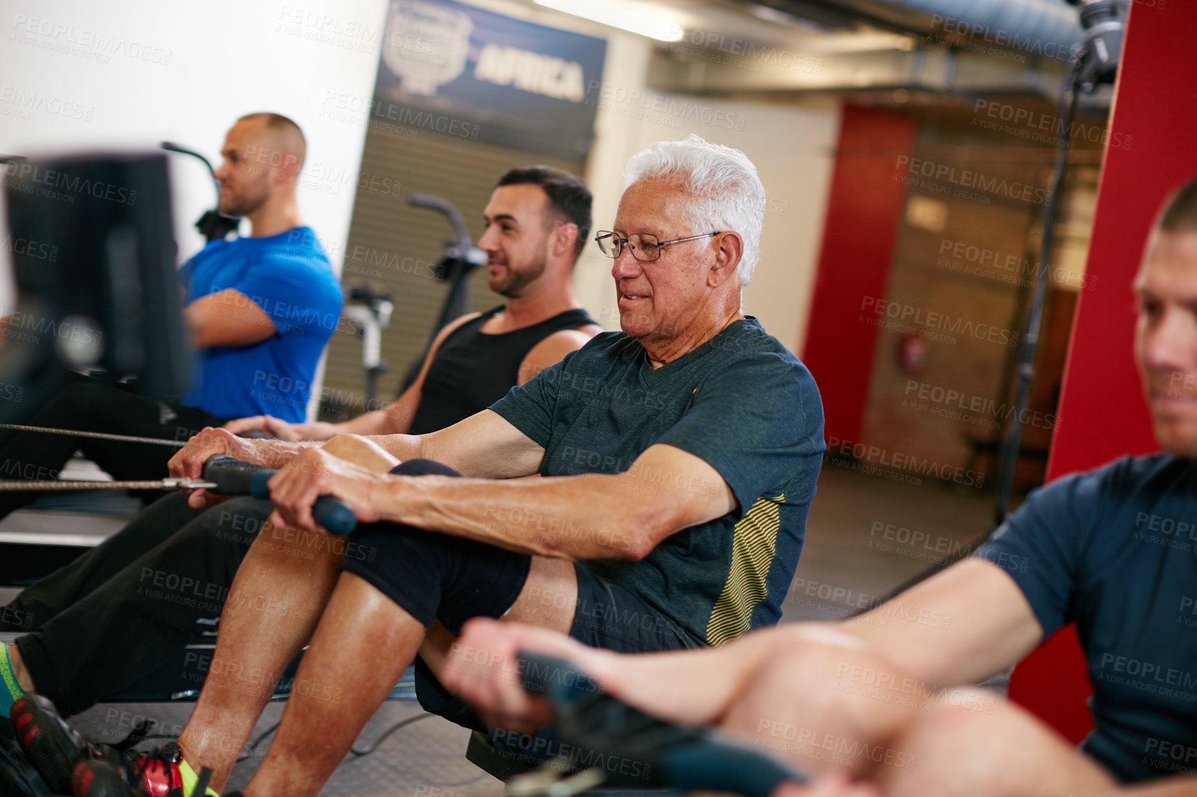 Buy stock photo Cropped shot of a group of men working out on the rowing machine at the gym