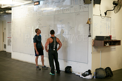 Buy stock photo Full length shot of two young men looking at a whiteboard while standing in the gym