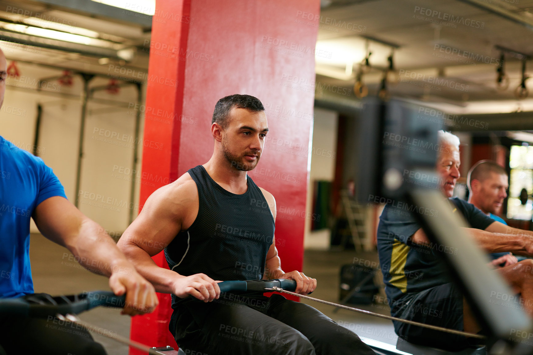 Buy stock photo Cropped shot of a group of men working out on the rowing machine at the gym