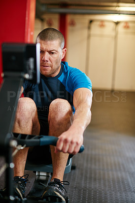 Buy stock photo Full length shot of a young man working out on the rowing machine at the gym