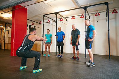 Buy stock photo Shot of a trainer demonstrating a squat workout at the gym
