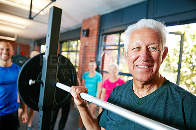 Buy stock photo Shot of a senior man lifting weights while a group of people in the background watch on