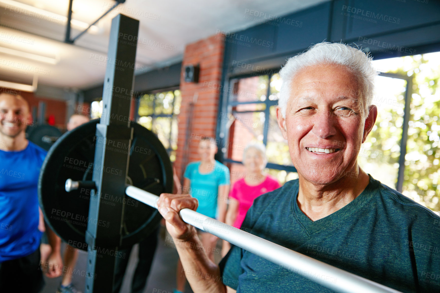 Buy stock photo Shot of a senior man lifting weights while a group of people in the background watch on