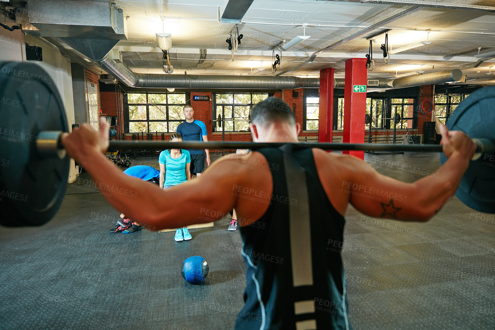 Buy stock photo Shot of a man lifting weights while a group of people in the background watch on