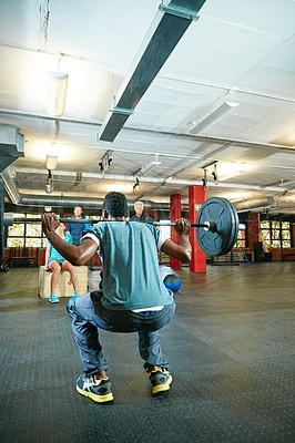 Buy stock photo Shot of a man lifting weights while a group of people in the background watch on