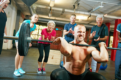 Buy stock photo Shot of a man lifting weights while a group of people in the background watch on