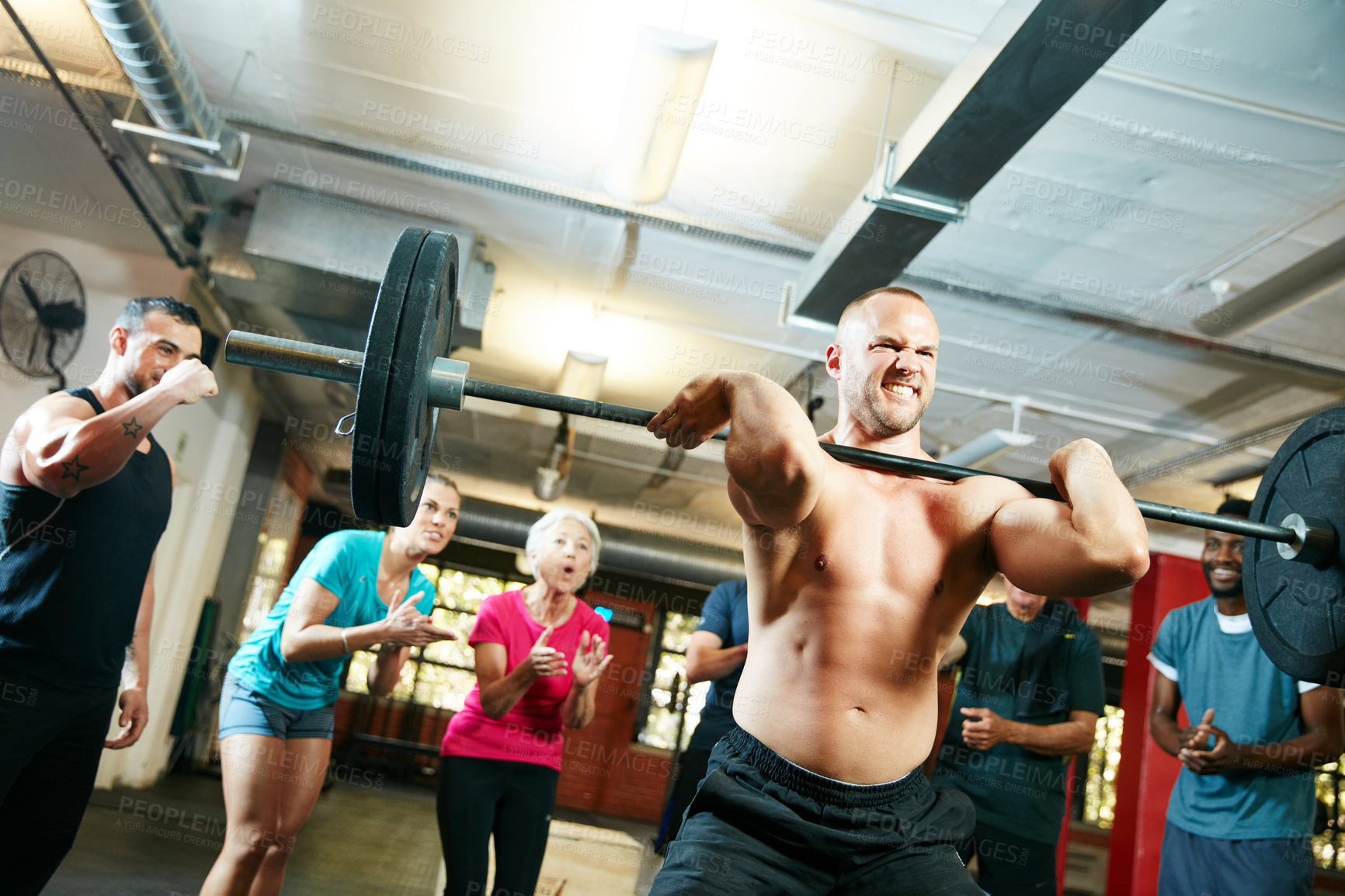 Buy stock photo Shot of a man lifting weights while a group of people in the background watch on