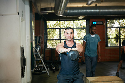 Buy stock photo Shot of a young man working out with a kettle bell at the gym