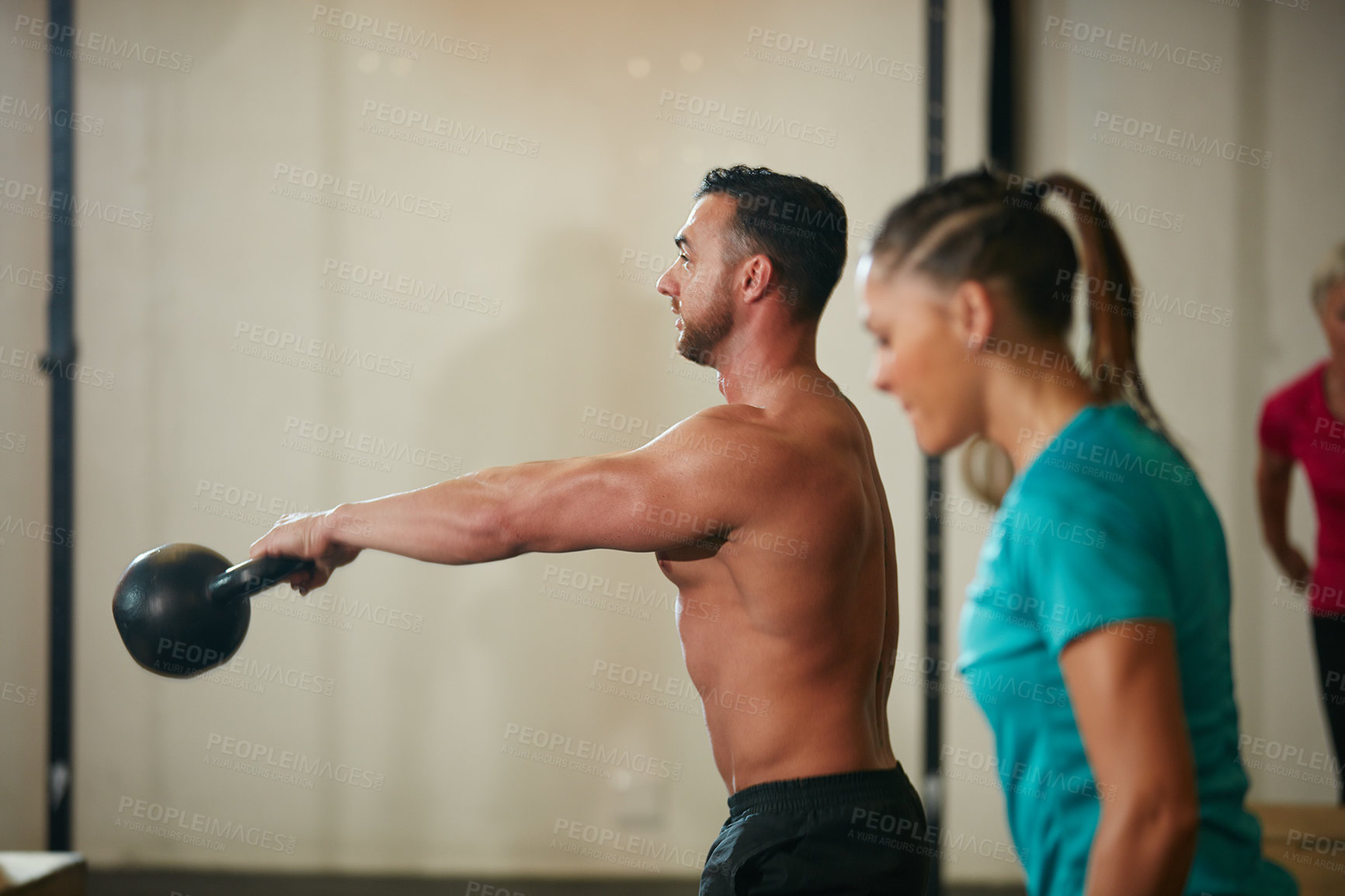 Buy stock photo Shot of a shirtless young man working out with a kettle bell at the gym