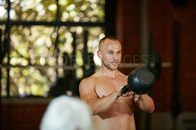 Buy stock photo Shot of a shirtless young man working out with a kettle bell at the gym