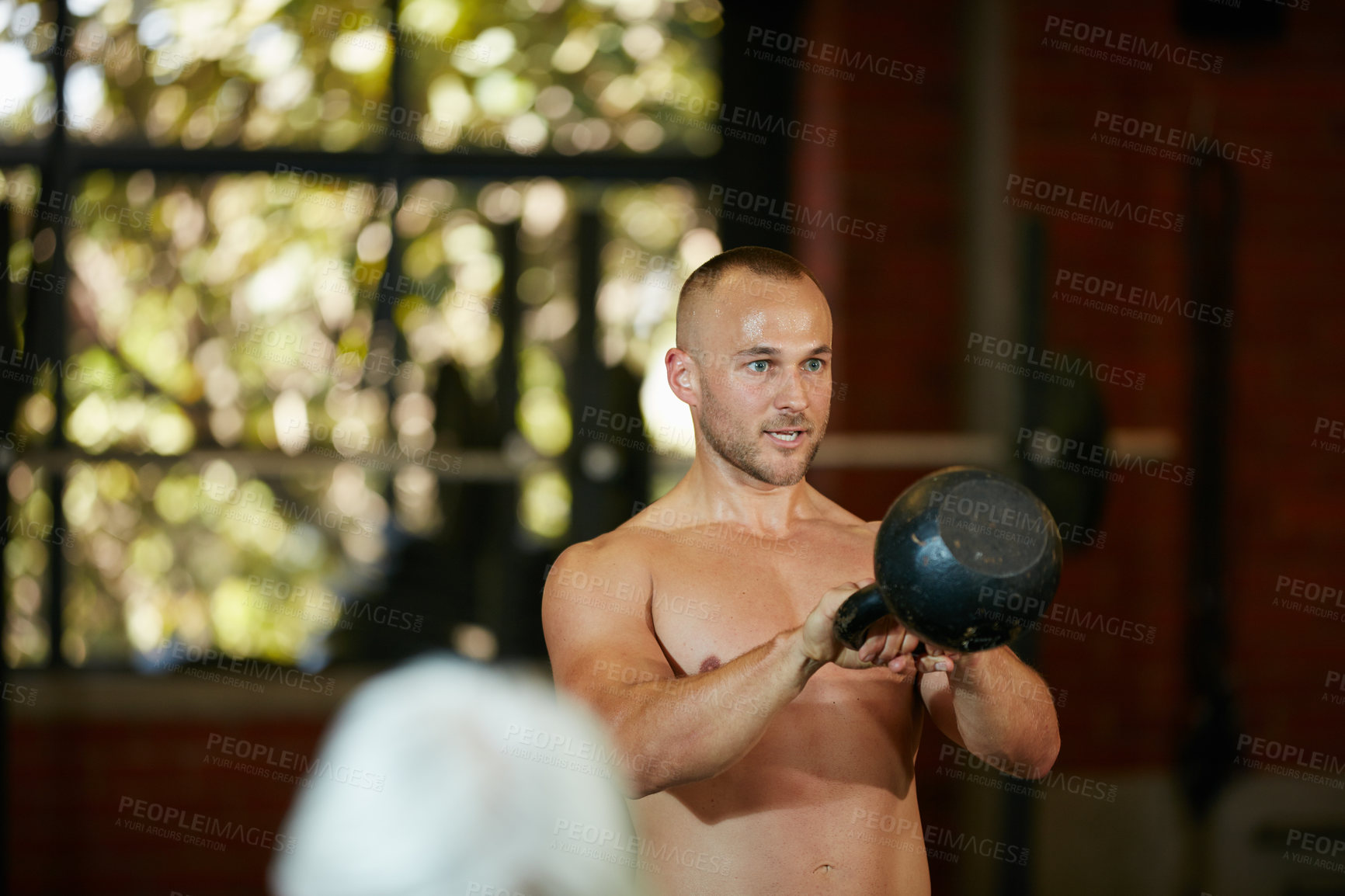 Buy stock photo Shot of a shirtless young man working out with a kettle bell at the gym