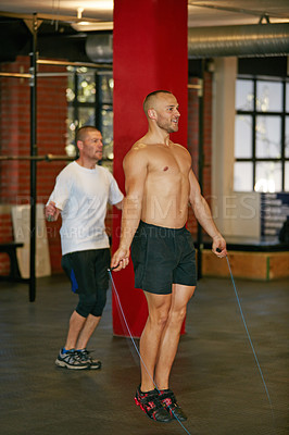Buy stock photo Shot of a shirtless young man skipping with a jumprope at the gym