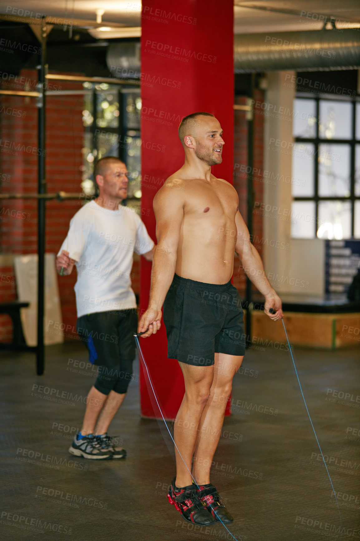 Buy stock photo Shot of a shirtless young man skipping with a jumprope at the gym