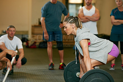 Buy stock photo Shot of a woman lifting weights while a group of people in the background watch on