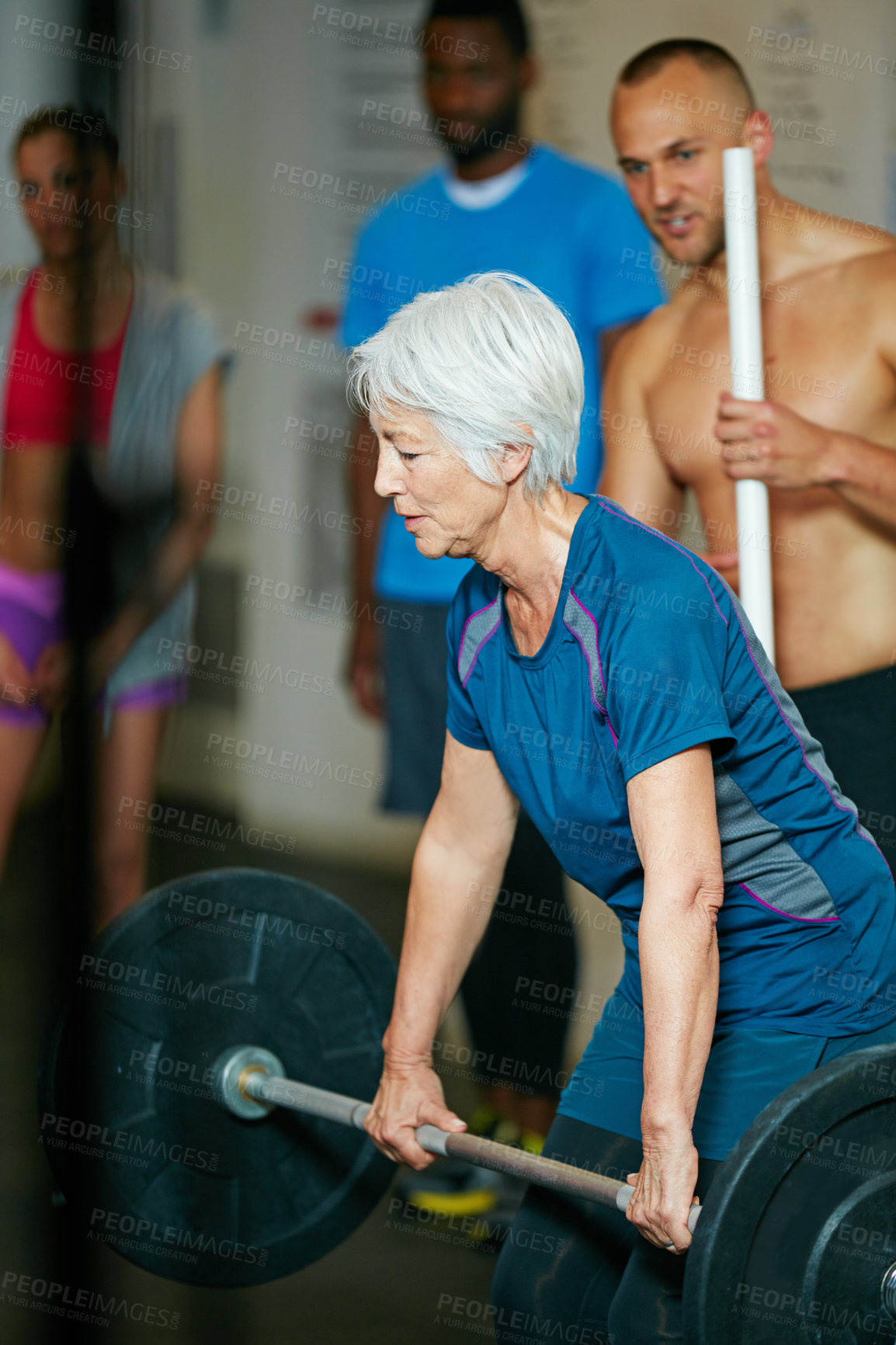 Buy stock photo Shot of a senior woman lifting weights while a group of people in the background watch on