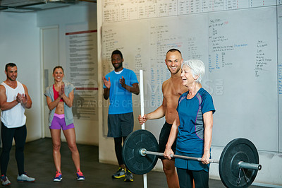 Buy stock photo Shot of a senior woman lifting weights while a group of people in the background watch on