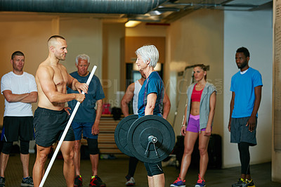 Buy stock photo Shot of a senior woman lifting weights while a group of people in the background watch on