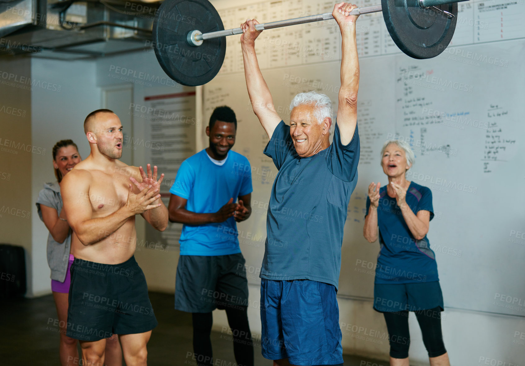 Buy stock photo Shot of a senior man lifting weights while a group of people in the background watch on