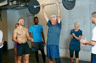 Buy stock photo Shot of a senior man lifting weights while a group of people in the background watch on