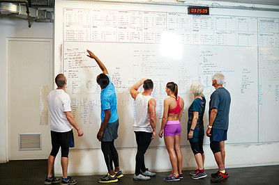 Buy stock photo Rearview shot of a group of people looking at a whiteboard while standing in the gym