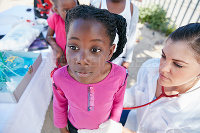 Buy stock photo Shot of a volunteer nurse examining a young patient with a stethoscope at a charity event