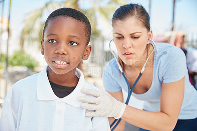 Buy stock photo Shot of a volunteer nurse examining a young patient with a stethoscope at a charity event