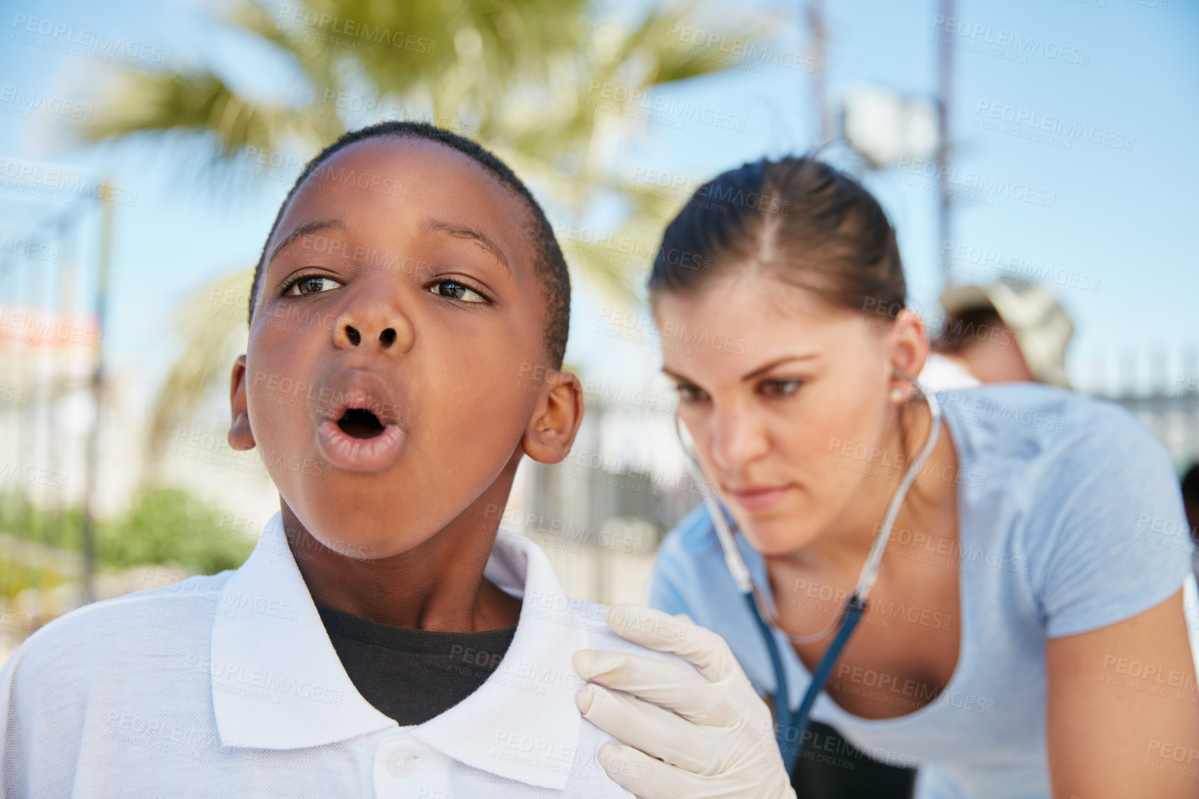 Buy stock photo Shot of a volunteer nurse examining a young patient with a stethoscope at a charity event