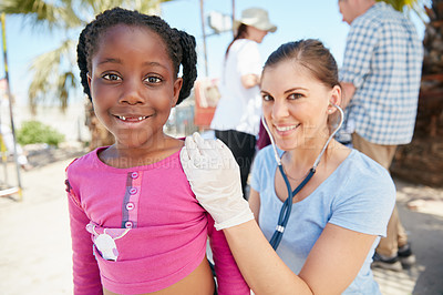Buy stock photo Shot of a volunteer nurse examining a young patient with a stethoscope at a charity event