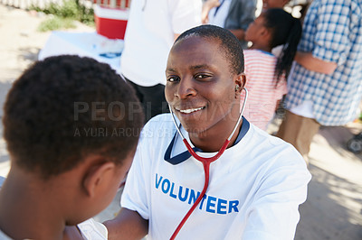 Buy stock photo Shot of a volunteer doctor examining a young patient with a stethoscope at a charity event