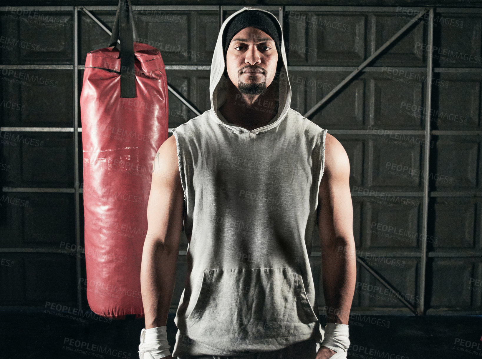 Buy stock photo Cropped portrait of a young male boxer standing in front of a punching bag