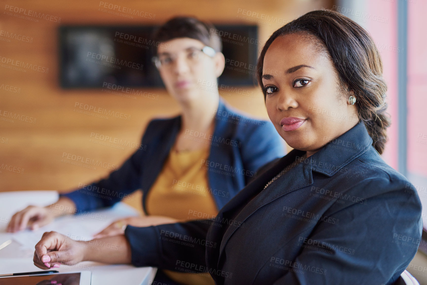 Buy stock photo Cropped portrait of a businesswoman sitting in the boardroom with a colleague in the background