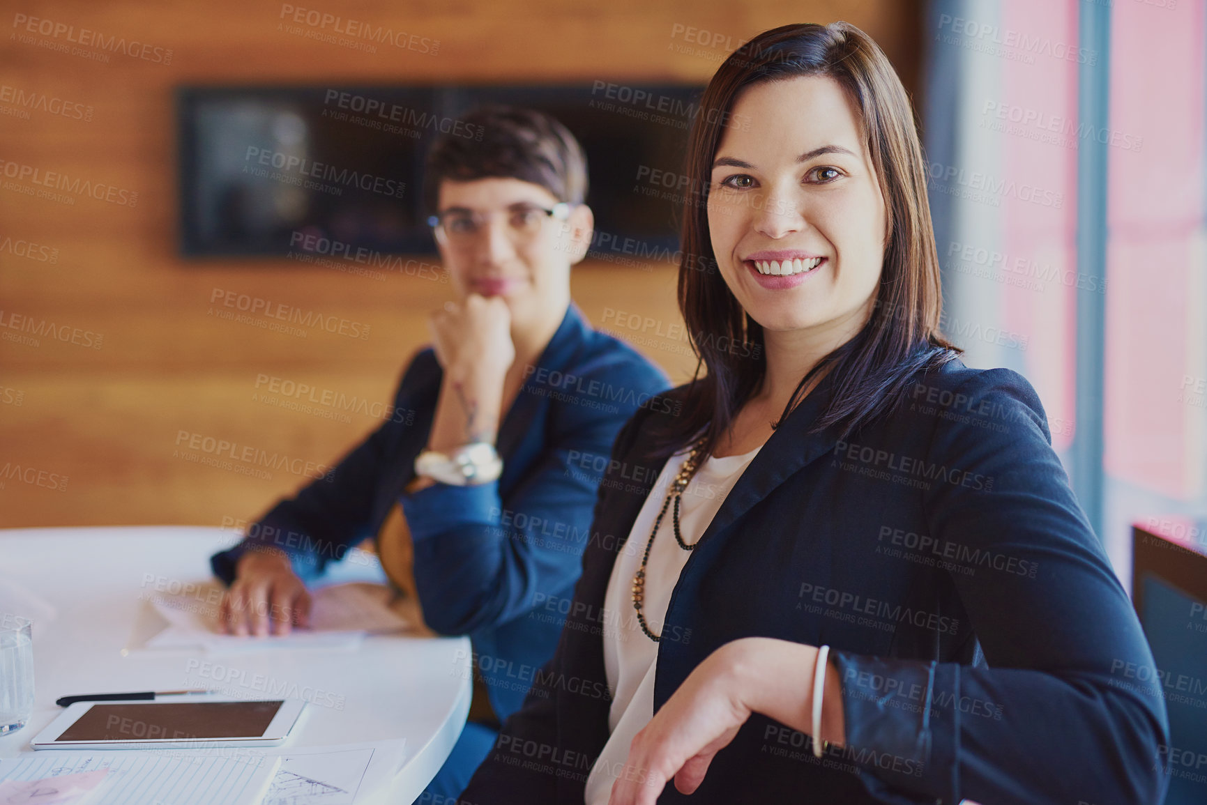 Buy stock photo Cropped portrait of a businesswoman sitting in the boardroom with a colleague in the background