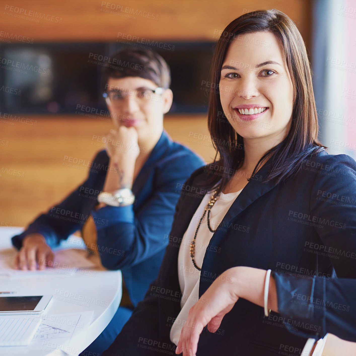 Buy stock photo Cropped portrait of a businesswoman sitting in the boardroom with a colleague in the background