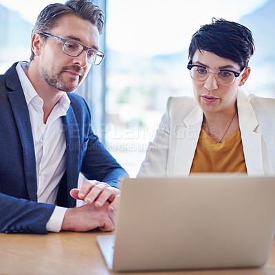 Buy stock photo Shot of two colleagues working on a laptop at a desk in an office