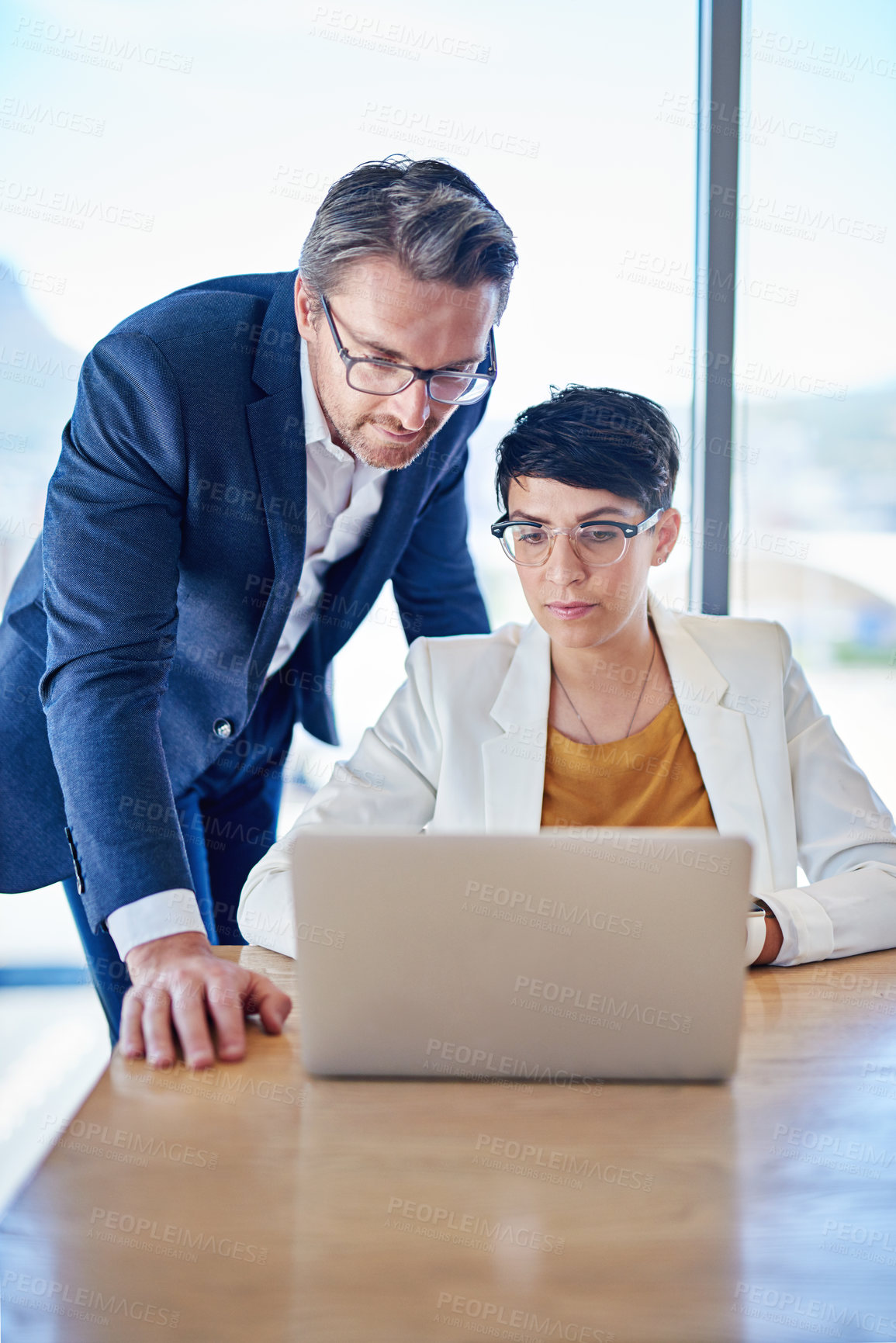 Buy stock photo Shot of two colleagues working on a laptop at a desk in an office