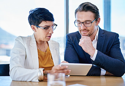 Buy stock photo Shot of two colleagues using a tablet together in an office