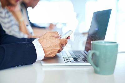 Buy stock photo Cropped shot of a businessman using his phone and laptop in an office