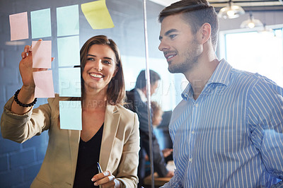 Buy stock photo Shot of coworkers arranging sticky notes on a glass wall during a brainstorming session