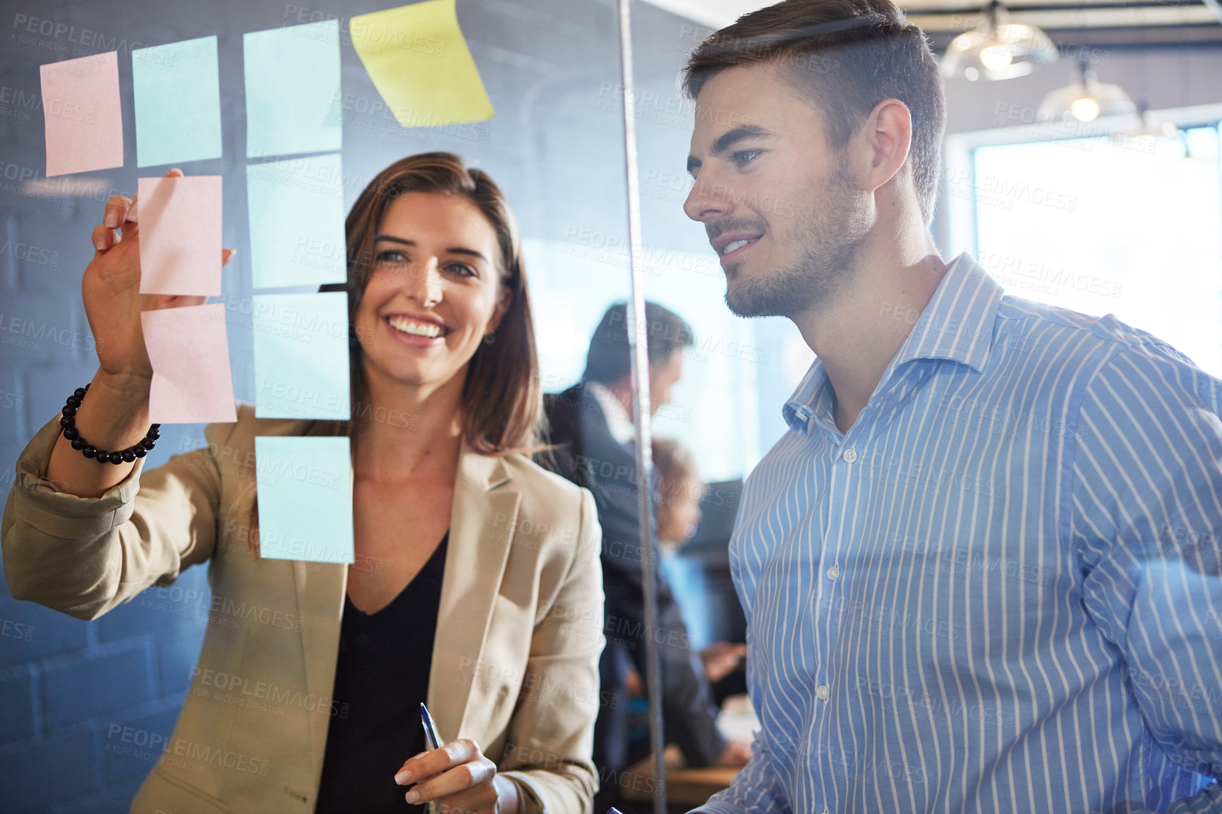 Buy stock photo Shot of coworkers arranging sticky notes on a glass wall during a brainstorming session