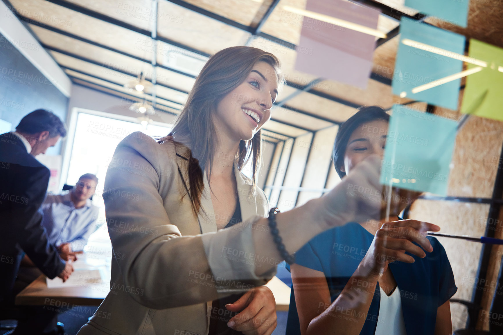 Buy stock photo Shot of coworkers arranging sticky notes on a glass wall during a brainstorming session