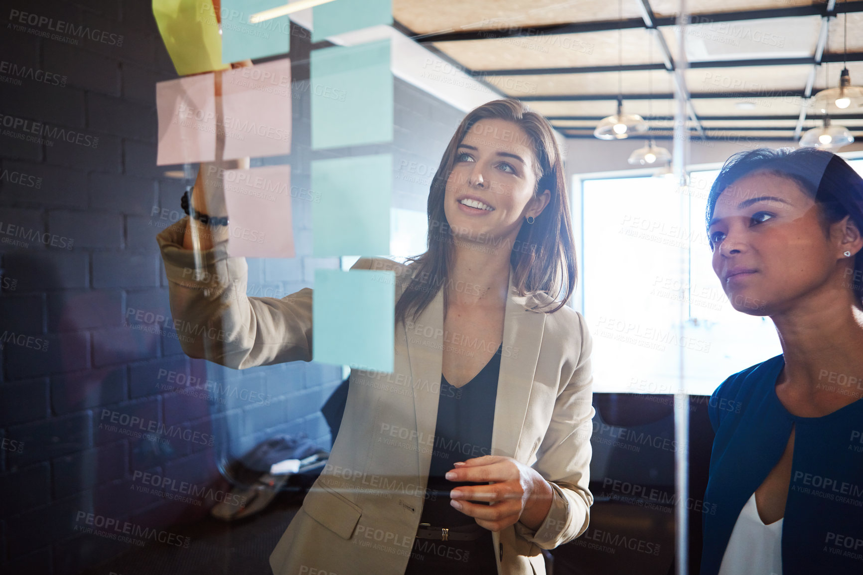 Buy stock photo Shot of coworkers arranging sticky notes on a glass wall during a brainstorming session